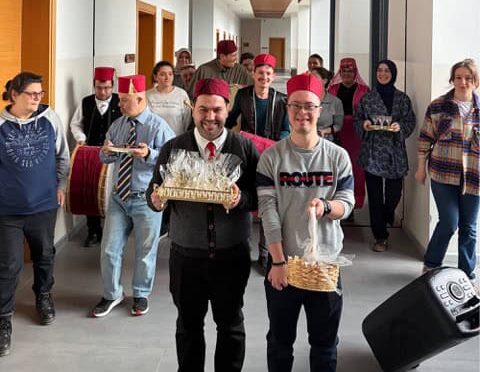 Kutlama yapan grup, ofis koridorunda, geleneksel kıyafetlerle ve gülümseyerek poz veriyor.